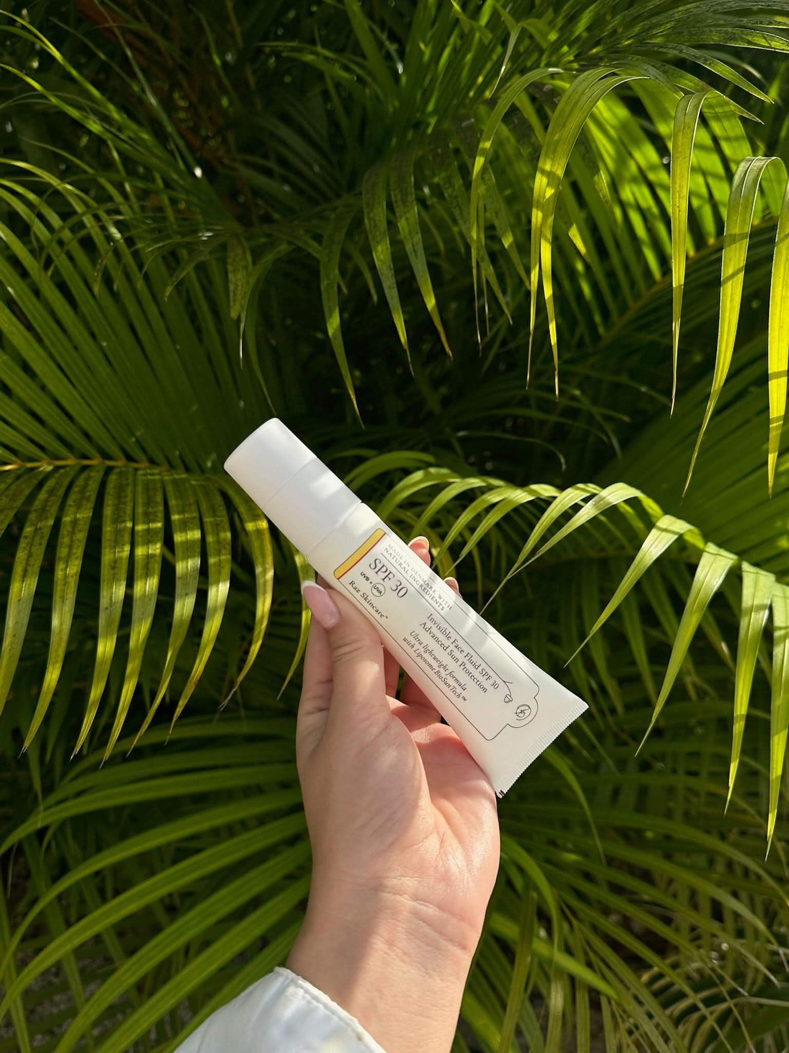 Verdens bedste solcreme med SPF30, hvor en hånd med neglelak på neglene holder den foran palmeblade