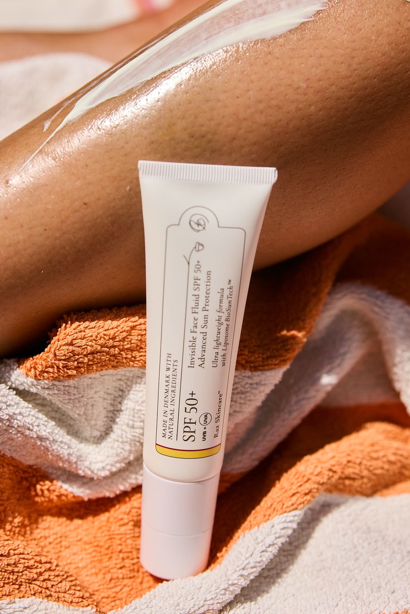 SPF50+ Invisible Face Fluid Solcreme 50ml standing on a towel in the sand with a leg in the background, with suncreen applied